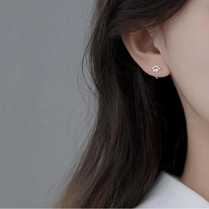 Close-up of small silver cat paw hook earrings worn by a model in a minimalist style