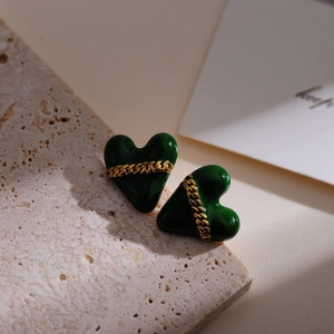 Macro shot of dark green heart earrings with gold chain detail on stone base