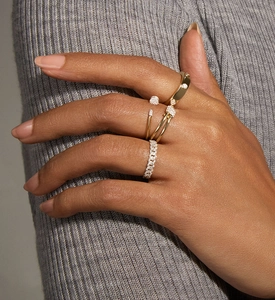 Close-up of layered gold rings with pavé diamonds on a grey knit texture background