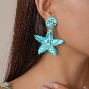 Close-up of blue beaded starfish earrings with pearl and crystal details on a model