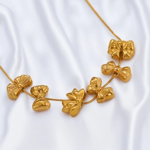 Golden stainless steel necklace featuring multiple bow-shaped charms on a white silk background