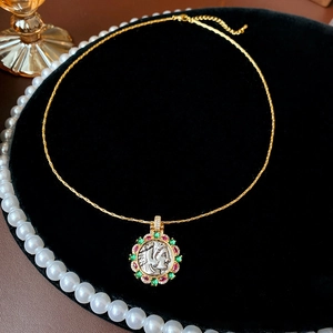 Close-up of gold coin pendant with colorful gemstones and vintage portrait detail