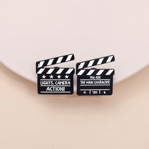 Creative clapperboard enamel pins featuring movie theme quotes on a beige and white background