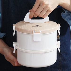 Dual-layer portable bento box with wooden style lid held by hands in a kitchen setting