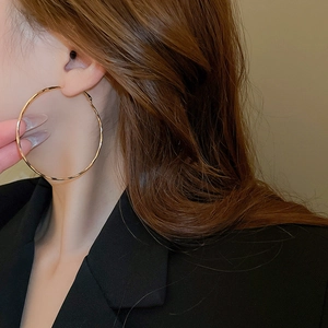 Close-up of model wearing large minimalist golden metal hoop earrings with high shine