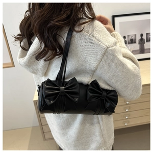 Détail d'un sac baguette cylindrique noir avec de grands nœuds sur un pull en maille