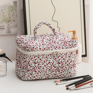 Quilted floral cosmetic bag with red flowers and top handle on a white desk