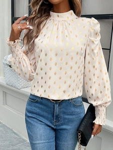 Detail of beige long sleeve blouse with golden polka dots and elastic cuffs on a model