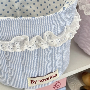Close-up of quilted stripe fabric basket with blue polka dot lining and lace trim edge