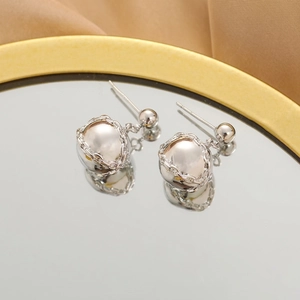 Close-up of silver ball stud earrings with decorative chain wrap on a mirror