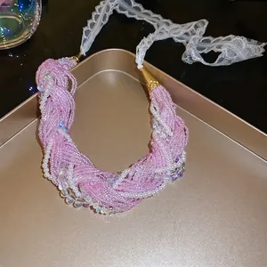 Pink beaded braided necklace with pearls and white lace ties on a golden tray