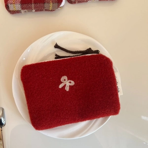 Macro shot of red wool felt coin purse featuring white bow embroidery and double tassels
