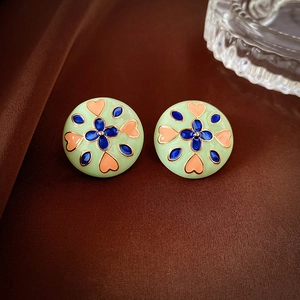 Detail of vintage-style enamel earrings with blue petals and orange heart patterns