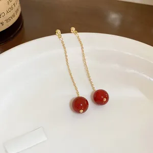 Makro-Detail langer goldener Quastenohrringe mit roten Perlen auf einem weißen Teller