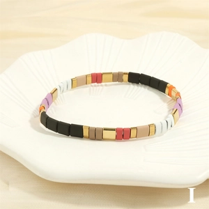 Detail of colorful enamel tile stretch bracelet with gold accents on ceramic tray