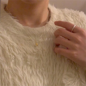 Close-up of minimalist gold heart necklace and textured silver ring on knit sweater