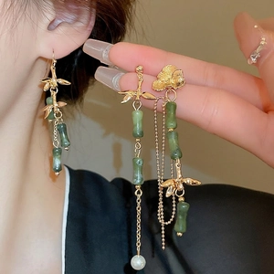 Bamboo style earrings with long gold tassels, green stones, and pearls on a model