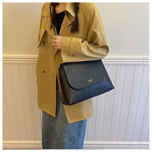 Detail of black crossbody chain bag with gold logo on beige trench coat outfit