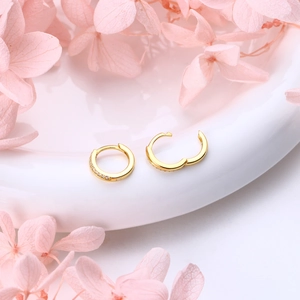 Détail de boucles d'oreilles créoles dorées serties de cristaux sur un plat en céramique