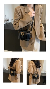 Detail of a black vanity bag with gold zippers and a decorative woven bell charm
