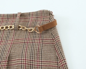 Detail view of high-waist houndstooth shorts with gold chain and zip closure