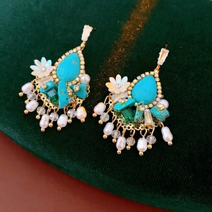 Dettaglio di orecchini floreali boho con turchese, perle e cristalli su velluto verde