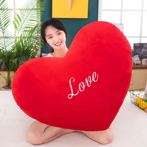Detail of a large red heart plush pillow with Love embroidery held by a model