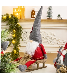 Close-up of plush Christmas gnome sitting on a wooden sled by a warm fireplace
