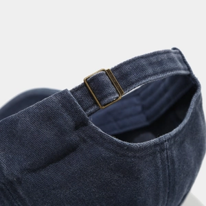 Macro detail of the navy washed cotton baseball cap with adjustable brass metal buckle strap