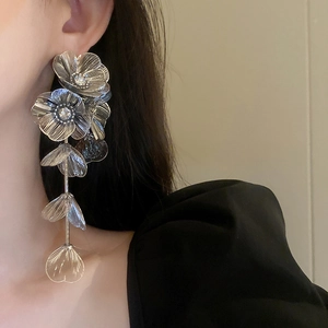 Close-up of oversized silver flower tassel earrings with intricate wire-woven design on model
