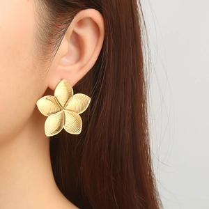 Golden flower-shaped stainless steel earrings worn by a model in a natural setting