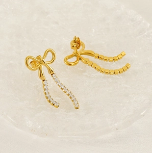 Detail view of elegant golden bow earrings with long sparkling tassel on a textured glass tray
