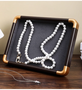 Macro detail of walnut jewelry tray with gold corners and grey velvet lining for pearls