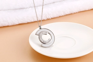 Macro shot of silver C-letter necklace with rhinestones and inlay on ceramic plate