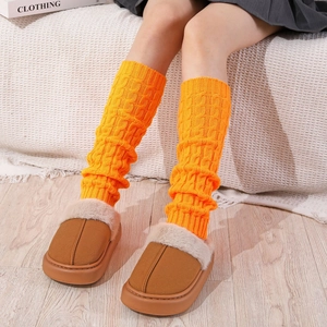 Close-up of bright orange thick knit leg warmers with textured twist cable patterns