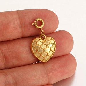 Macro shot of 18K gold heart pendant with fish scale texture held by fingers