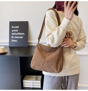 Brown corduroy shoulder bag with front pocket shown on a model in a cozy home setting