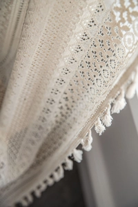 Detail of ivory crochet lace curtain showing intricate hollow patterns and soft fringe trim