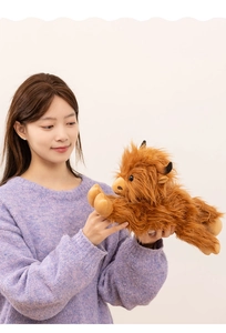 Close-up of fluffy brown Highland cow plush toy held by a model in a warm home setting