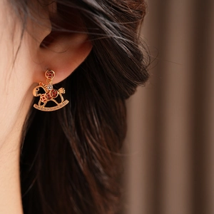 Close-up of gold rocking horse earring with red enamel and crystals on model ear