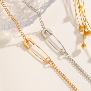 Detailed view of silver and gold safety pin pendant necklaces on a textured glass surface