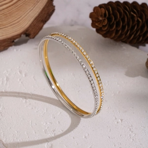 Set aus Gold- und Silber-Edelstahlarmbändern mit funkelnden Kristallen auf weißem Stein