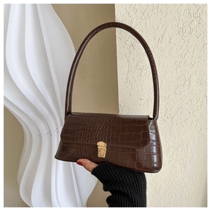 Detail of dark brown crocodile pattern handbag with gold clasp on white pedestal