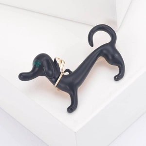 Detail of dachshund brooch with green gemstone eyes and gold bow tie on white stand