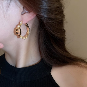 Close-up of gold-plated hoop earring with pearl accents and CD logo on a female model