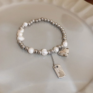 Detail of pearl bracelet with silver beads, heart charm and engraved ID tag on a ceramic tray