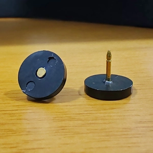 Detail of black round magnetic stud earrings with gold pins on wooden surface