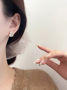 Close-up of golden gourd-shaped earrings with clear zircons worn by a model