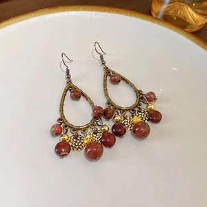 Gros plan de boucles d'oreilles bohèmes en forme de goutte avec perles rouges sur assiette