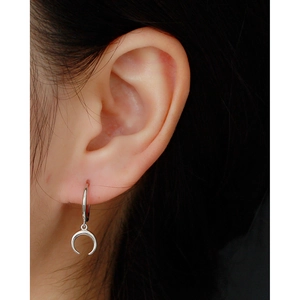 Close-up of a silver crescent moon pendant earring worn on a model's earlobe